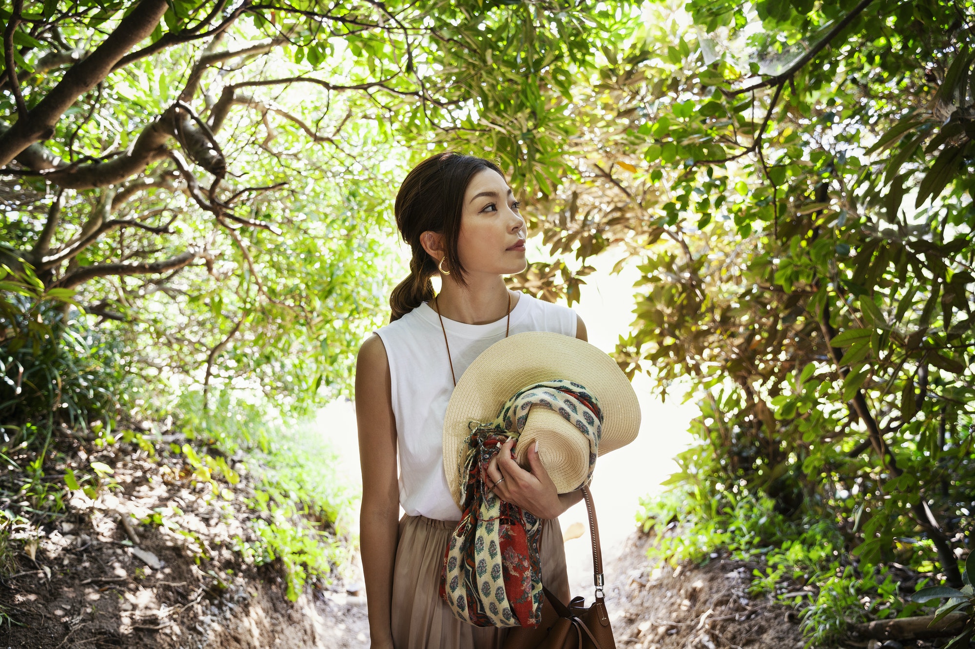 Japanese woman carrying hat hiking in a forest.