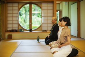Two Japanese women and Buddhist priest kneeling in Buddhist temple, praying.